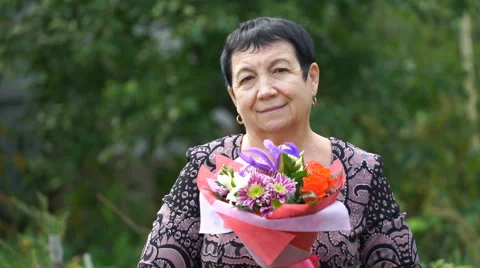 Footage elderly woman holding a bouquet of flowers outdoors. 4K Stock Footage