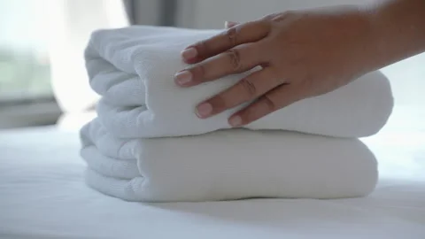 Footage of a woman's hand placing a stack of fresh white towels on the bed. Stock Footage 275367601