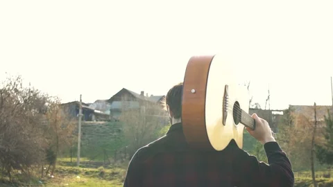 Footage young guy walks at the rays of the sunset with guitar. Stock Footage 109180023