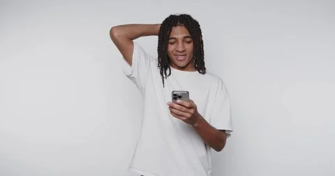 Footage of young man stands casually, enjoying his smartphone on light back.. Stock Footage 314773601