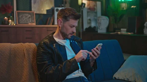 Footage of young smiling bearded man sitting on sofa and touching screen of Stock Footage 238740294