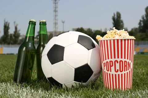 Football ball with beer and popcorn on green field grass in stadium Stock Photos