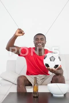 Football fan sitting on couch with ball cheering Stock Photos