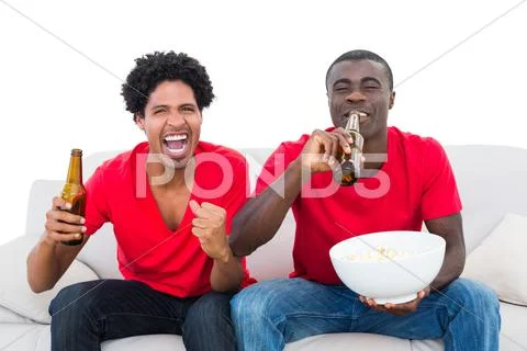Football fans in red cheering on the sofa with beers and popcorn Stock Photos