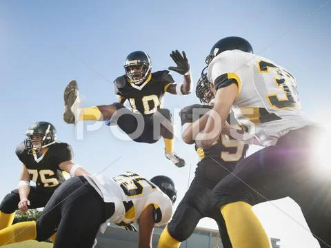 Football player leaping over players on football field Stock Photos
