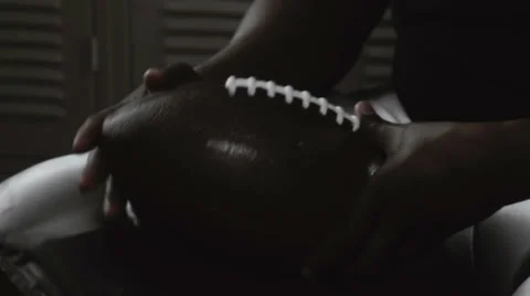 A football player plays with a ball while he sits in the locker room Stock Footage 33864042