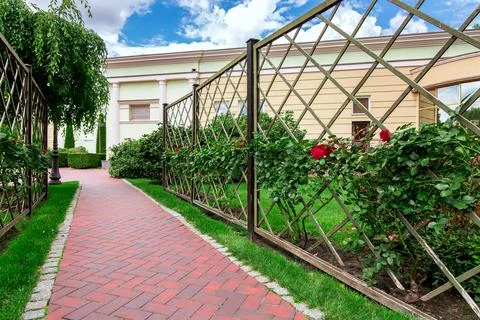 A footpath made of paving slabs surrounded by a green lawn and a fence. Stock Photos
