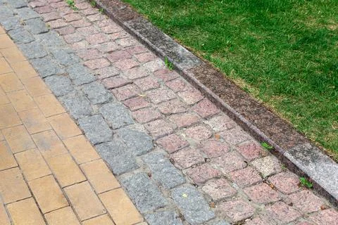 A footpath made of tiles of different types of stone and a granite curb. Stock Photos