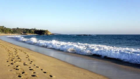 Footprints on the beach, waves and a cliff in the background Stock Footage 266440294