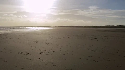 Footprints cover a sandy beach, under a setting sun, by the sea shore Stock-Footage 73543608