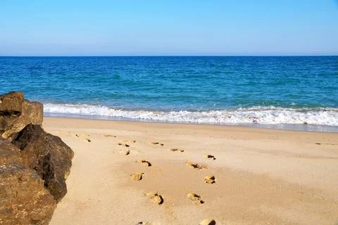 Footprints on an empty sandy beach, large stones on the shore, sea horizon an Stock Photos