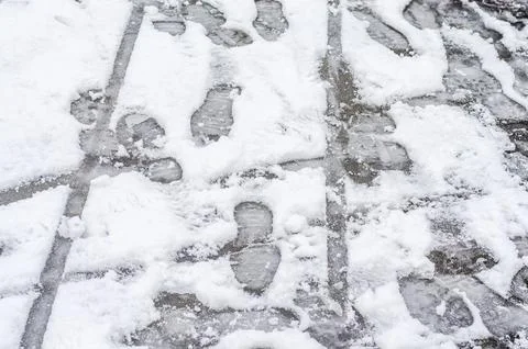 Footprints on a grid patterned stone pavement covered in snow. Stock Photos