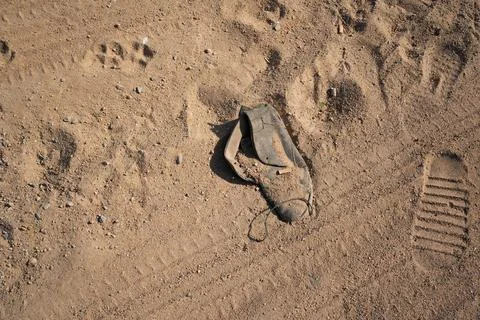 Footprints in the sand with a lost worn out shoe next to them Stock Photos