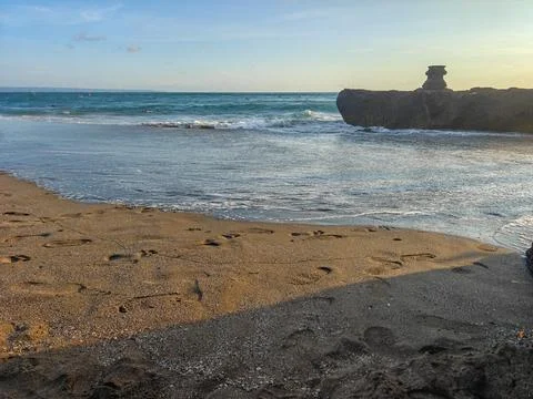 Footprints on sandy beach with ocean waves and rocky coast in Bali during sunset Stock Photos