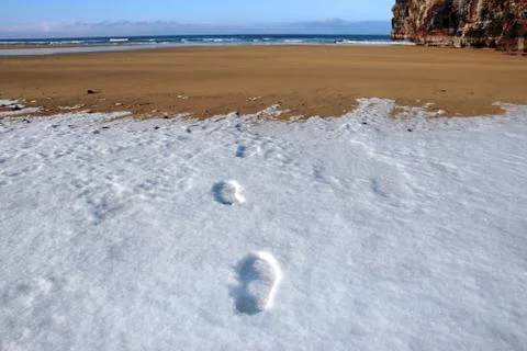 Footprints in snow on empty beach on a cold winters day Stock Photos