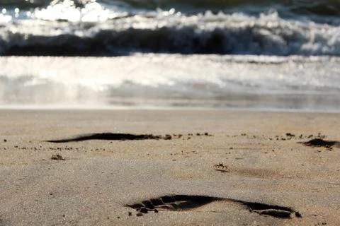 Footprints in the Soft Sandy Beach Accompanied by Ocean Waves in the Background Stock Photos