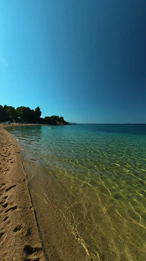 Footprints trail gently where waves lap the shore. Lagomandra, Greece. Vertical Stock Footage 339625680