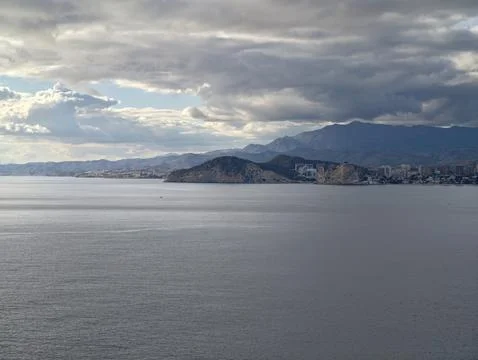 Foreboding storm clouds assemble over quiet coastal village against rugged Stock Photos
