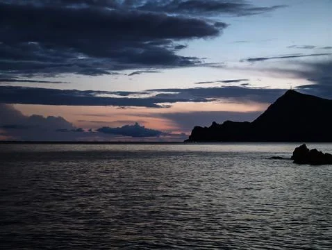 Foreboding weather over jagged coastline highlighted by subdued sunset shades Stock Photos