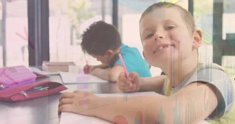 Foreground boy drawing then noticing camera, shifting posture and smiling, with Stock Footage 334316175