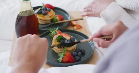 Foreground diner is placing fork and knife onto pancakes on bed tray, slicing Stock Footage 344402180