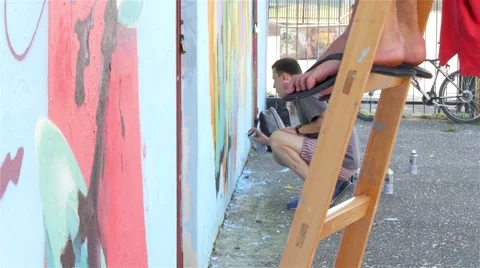 In foreground legs on ladder, in background guy spraying graffiti on the wall,4k Stock Footage 54758089