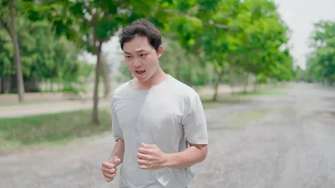 In the foreground, a tan Asian man is jogging on a jogging track in a park  Stock Footage 283187089