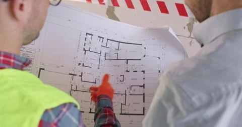 Foreman and colleague study paper floor plan during renovation Stock Footage 309928642