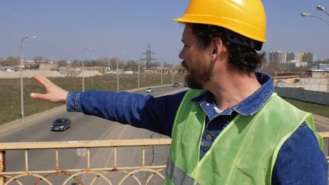 A foreman with a beard and mustache stands on the bridge wearing a yellow helmet Stock Footage 106356456