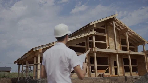Foreman Builder in helmet standing with his back to a wooden house Stock Footage 126707896