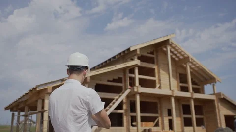 Foreman Builder in helmet standing with his back to a wooden house Stock Footage