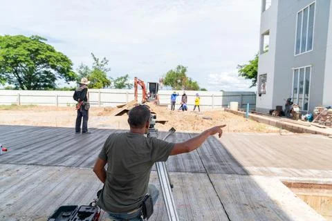 Foreman gives signal to worker while looking through level measuring device. Foto stock