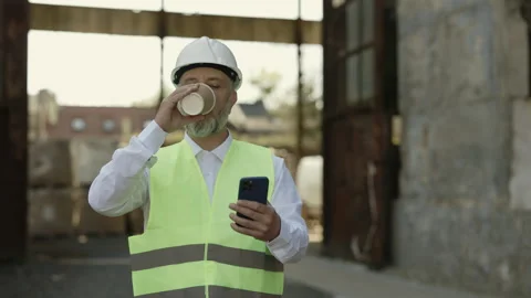 Foreman with mobile drinking coffee while walking at work Stock Footage 200068672