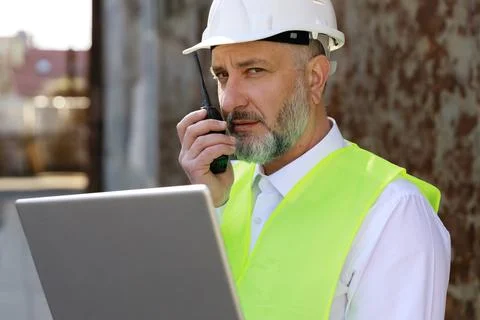 Foreman in protective hardhat looking at laptop and talking by walkie talkie Stock Photos