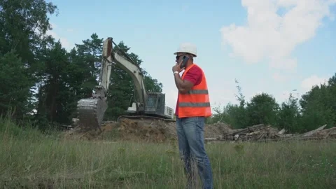 Foreman talks on phone against working excavator on construction site Stock Footage 169539694