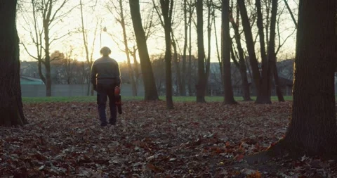 Foreman in uniform using blower for removing leaves at park Stock Footage 253194207