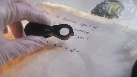 A forensic detective's hand holding a magnifying glass examines a Stock Footage 267213600