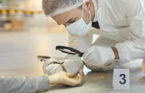Forensic expert examining corpse hand with magnifying glass collecting evidence Stock Photos