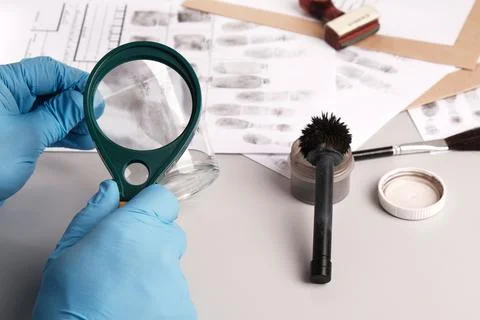 Forensic expert using  magnifying glass examines fingerprints on evidence -   Foto stock