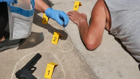 Forensic inspector collecting firearm shells at a crime scene with a dead male Stock Footage 157807307