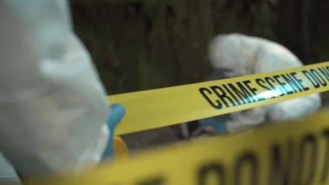 A forensic scientist rolling out police tape at a crime scene at night Video stock 283865628