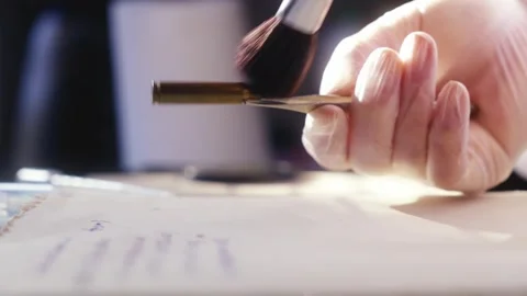 A forensics expert examines the bullet, working with a brush and Video stock 268403813