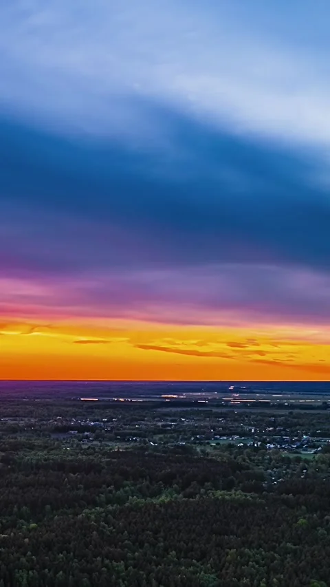 Forest and homes below blue, pink and orange clouds, vertical aerial hyperlapse Stock Footage 348794858