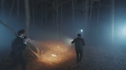 In forest detectives young men running at night with flashlight. Security 動画素材 175410413