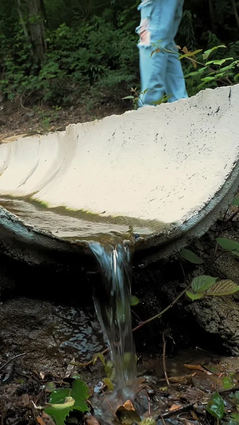 Forest drainage system. Water flowing through the channel. A tourist stepping Stock Footage 313729386