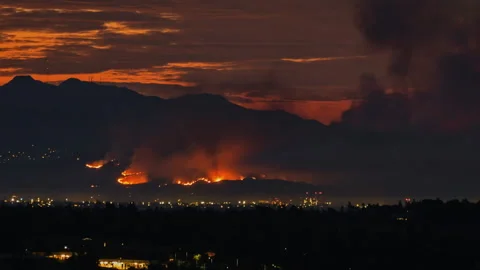 Forest fire burning on a mountain at night transitioning into sunrise Vídeos de archivo 332961381