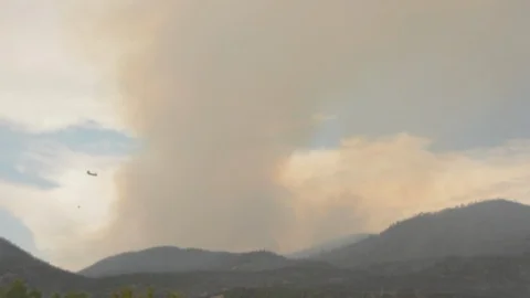Forest fire on a mountain behind town, large plumes of smoke hang overhead. Stock Footage 92605888