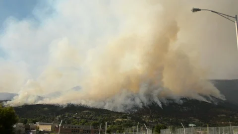 Forest fire on a mountain behind town, large plumes of smoke hang overhead. Stockbeeldmateriaal 92606123