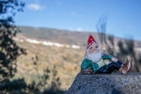 Forest gnome with red cap lying posing on a stone in the field Stock Photos