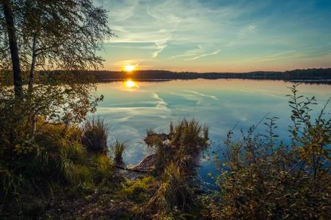 The forest lake at sunset, with reflection of sky and forest on a water smoot Stock Photos